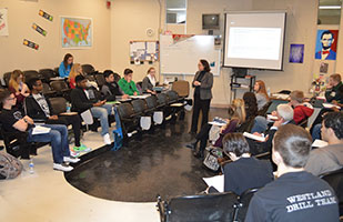 Image of a woman in a business suit speaking to a classroom of students
