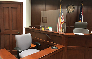 Image of a judge's bench showing plexiglass installed as a barrier between the bench and the witness stand