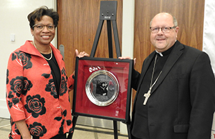 Image of Ohio Supreme Court Justice Melody Stewart standing next to a priest and a silver, framed award on an easel