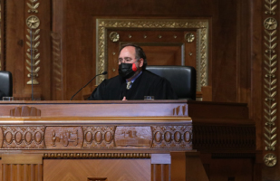 Image of a male judge wearing a black judicial robe and a mask on the bench in the courtroom of the Thomas J. Moyer Ohio Judicial Center
