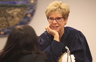 Image of a female judge with her chin resting on her hand speaking to another woman