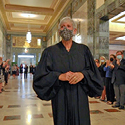 Woman in a black judicial robe surrounded by more than 100 people applauding in a marble hallway.