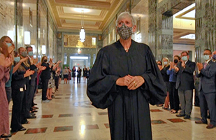 Woman in a black judicial robe surrounded by more than 100 people applauding in a marble hallway.