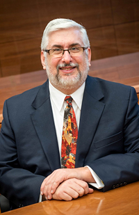 Bearded man wearing glasses, a suit, and tie.