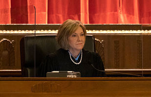 Woman in black judicial robing sitting and watching from a judge's bench.