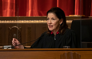 Image of a female judge wearing a black judicial robe sitting on the bench in the courtroom of the Thomas J. Moyer Ohio Judicial Center