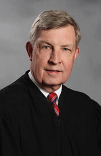 Image is a headshot photo of Judge Carroll in his black judicial robe