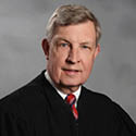 Image is a headshot photo of Judge Carroll in his black judicial robe
