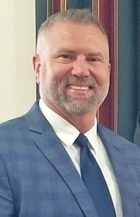 Image of a man with a beard wearing a blue checkered suit smiling