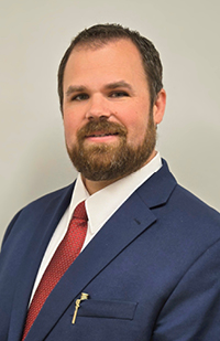 Image of a man wearing a blue suit jacket, white dress shirt, and red tie.