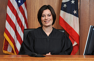 A female judge with short, dark hair, wearing a black judicial robe.