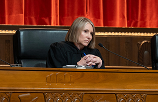 A woman wearing a black judicial robe seated behind a wooden bench in the courtroom of the Thomas J. Moyer Ohio Judicial Center.