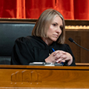 A woman wearing a black judicial robe seated behind a wooden bench in the courtroom of the Thomas J. Moyer Ohio Judicial Center.