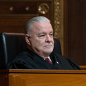 A male judge sitting at a courtroom bench wearing a black judicial robe.