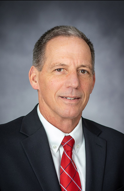 A man wearing a navy blue blazer, white dress shirt, and red tie.