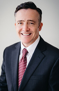 A man wearing a dark blue suit coat, white dress shirt, and red and white polka dot tie.