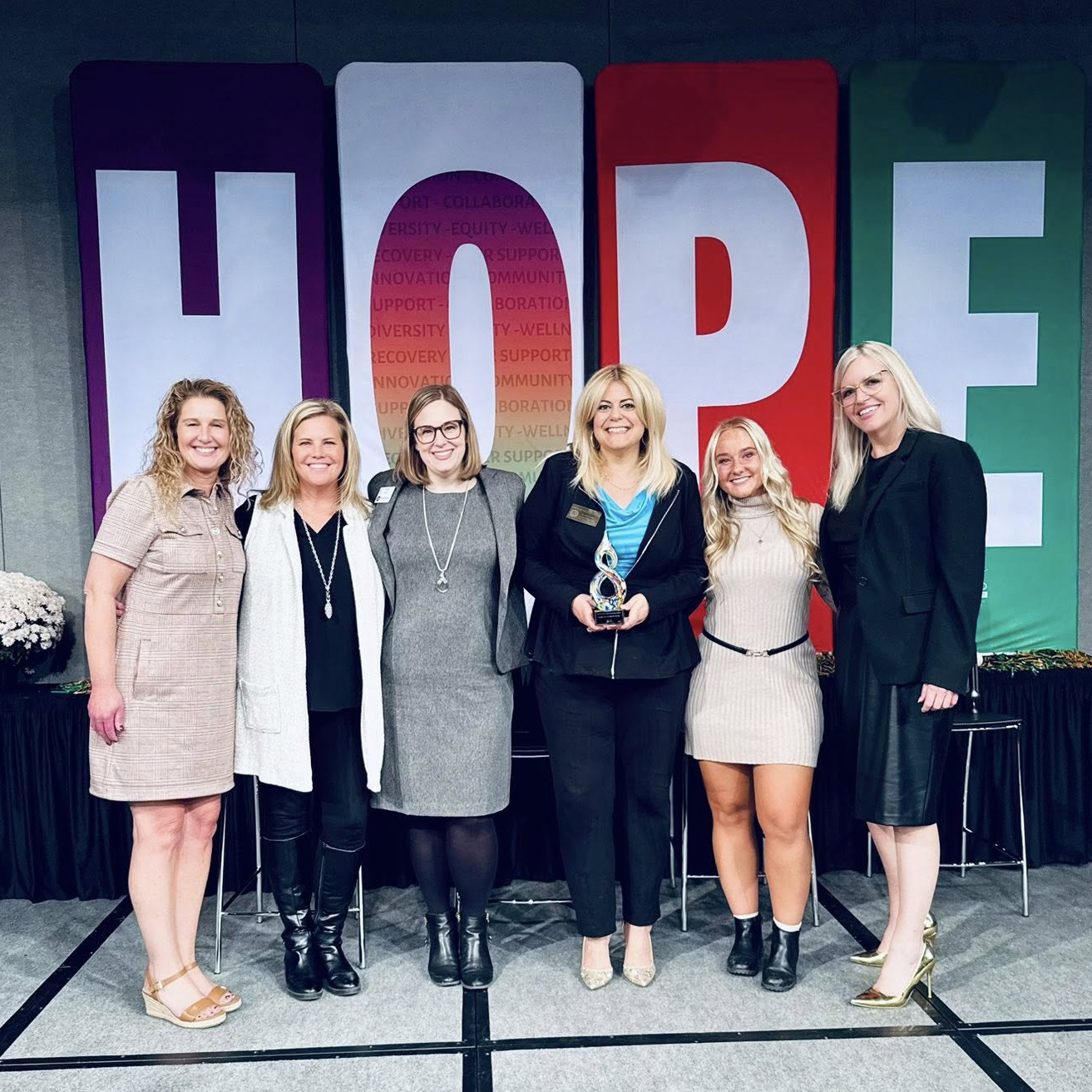 Six women smiling, one holding an award