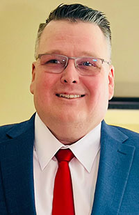 A man wearing a blue suit, white dress shirt, and red tie.