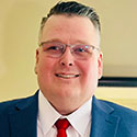 A man wearing a blue suit, white dress shirt, and red tie.