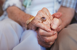 A closeup image of an elderly couple holding hands