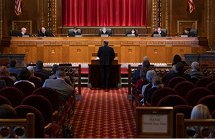 Image of an attorney standing at a lecturn addressing the Chief Justice and Justices sitting on the bench in the courtroom of the Thomas J. Moyer Ohio Judicial Center