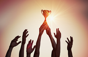 Image of several arms raising a trophy into the air (vchal/iStock)
