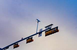Image shows a traffic camera mounted on a horizontal pole alongside traffic lights