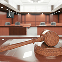 Close-up image of a wooden gavel sitting on a table in front of an empty courtroom