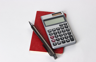 Image of a calculator and a pen sitting on top of a small, red notebook