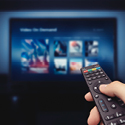 Image of a hand holding a television remote control pointed at a flat screen tv