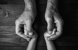Black and white image of a man's hands holding the hands of a child