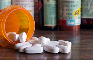 Image of several prescription bill bottles. One bottle is tipped over and pills are spilling out.