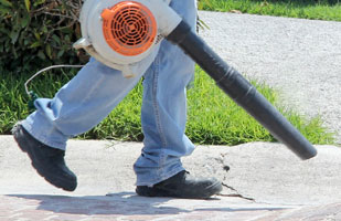Image of a man's legs walking carrying a leaf blower.