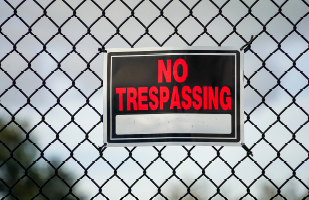 Image of a 'No Trespassing' sign attached to a chain link fence.