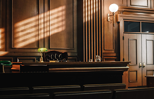 Image showing a dimly lit courtroom and an empty judicial bench.