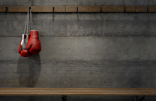 A pair of red and white boxing gloves hanging by their laces from a hook above a wooden bench.