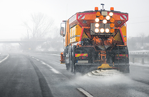 An orange snow plow releasing salt on a highway.