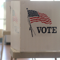 Image of a white privacy screen on top of a small table. The screen has an American flag and the word 'Vote' on it.