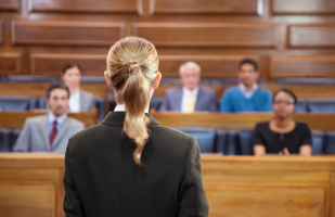 Image of a woman wearing a black suit facing a group of men and women seated in a jury box.