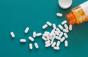 A prescription pill bottle on its side with white pills spilling out.