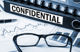 A black binder with the word 'confidential' written on its spine next to a pair of glasses, both laying on top of a line graph.