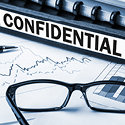 A black binder with the word 'confidential' written on its spine next to a pair of glasses, both laying on top of a line graph.