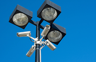 A light pole with three lights and four surveillance cameras.