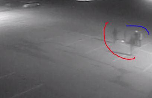 Grainy surveillance image of several people standing in an empty parking lot at night.