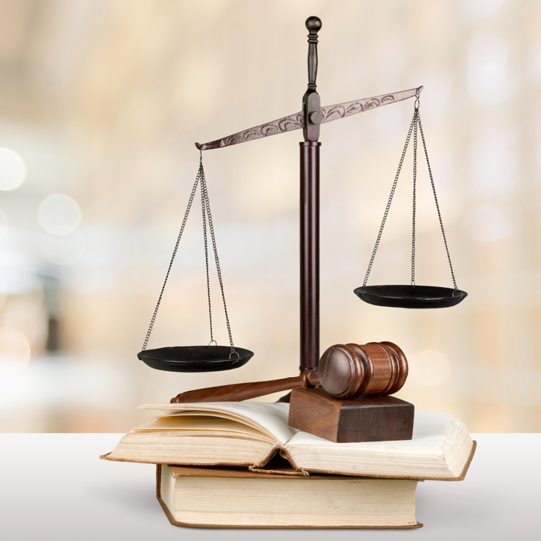 Scales of justice and a wooden gavel and sound block on top of some law books.