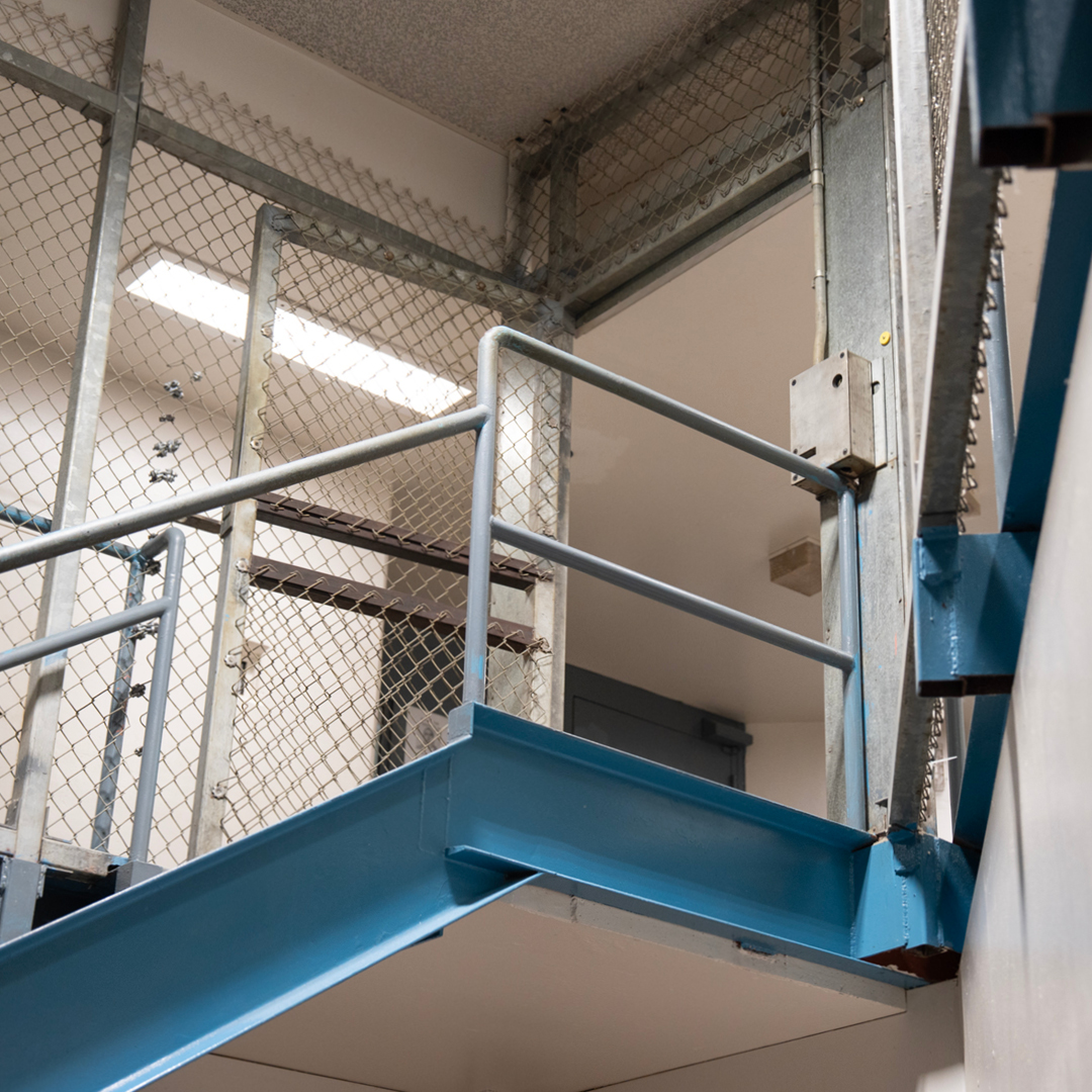 A metal staircase leading to an area confined by chain link fencing in a prison.