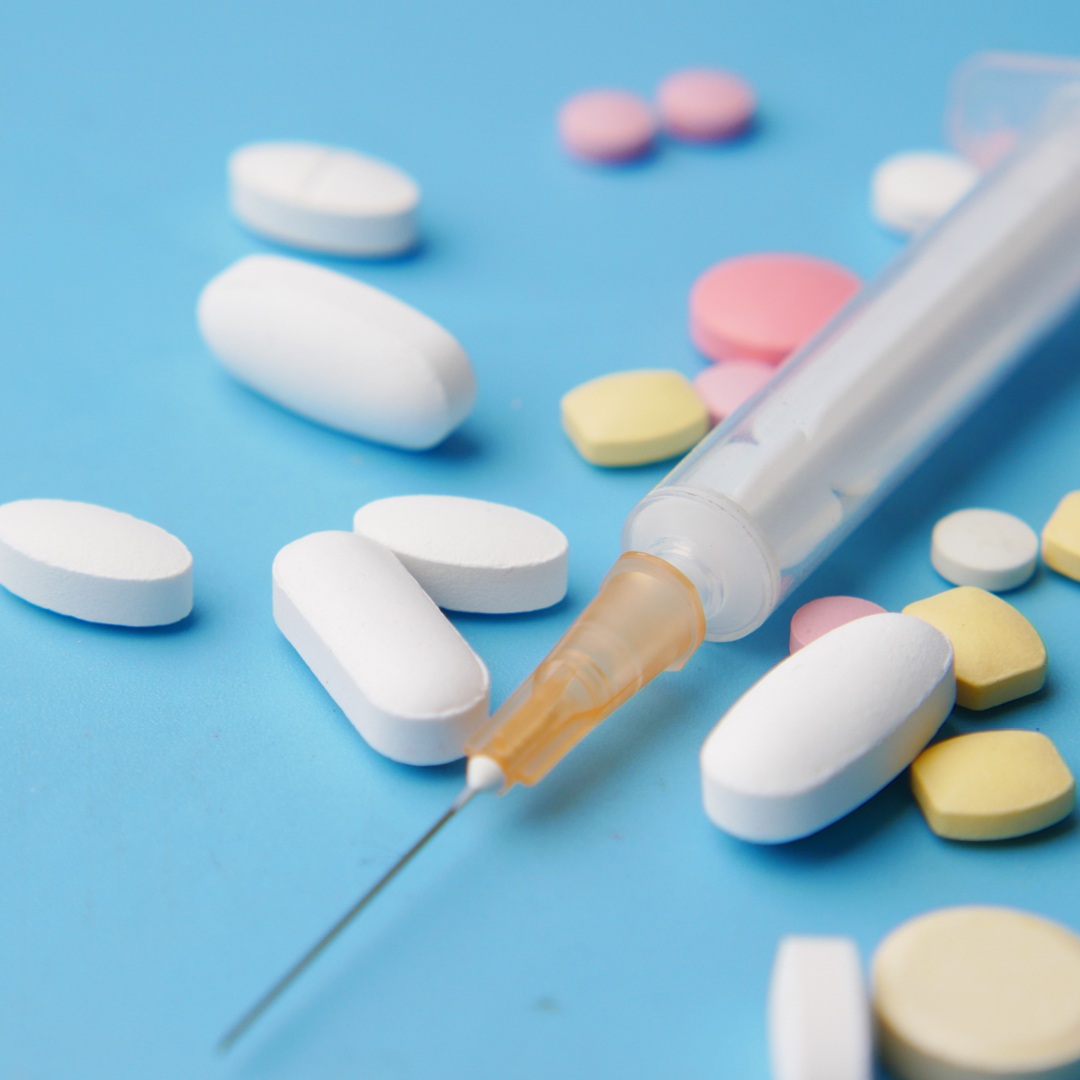 A syringe surrounded by pills of varying shapes, sizes, and colors