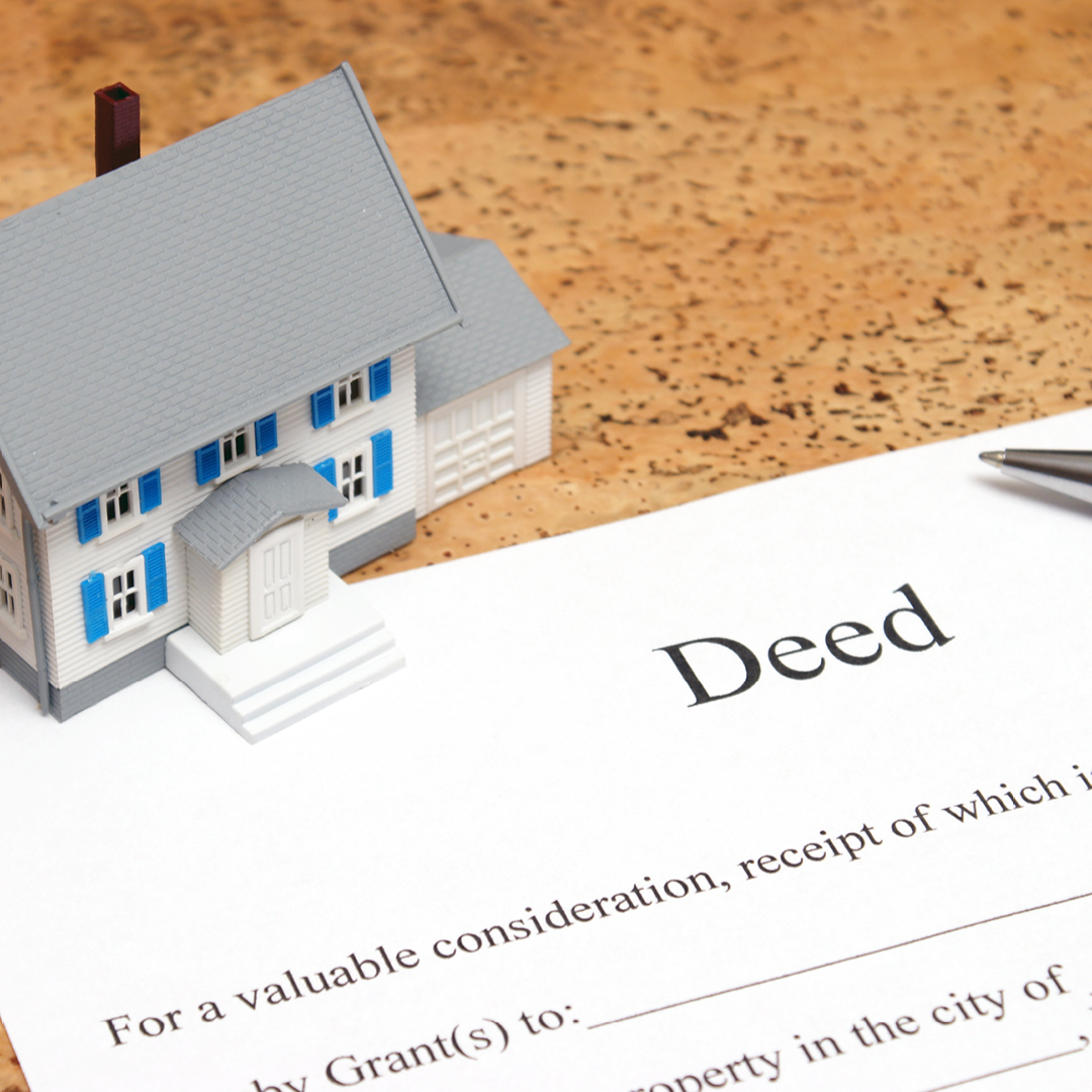 A tiny toy house placed on top of a paper with the word 'Deed' at the top