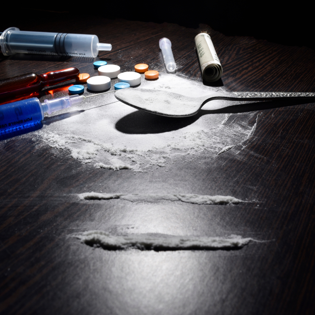 A spoon, syringe, various pills, and a white powdery subsdance on a table