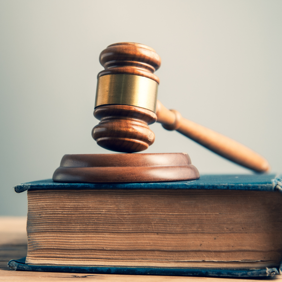 An image featuring a wooden gavel resting on a sound block, which is placed on top of a thick, blue legal book.
